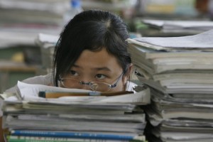 A middle school student sits behind a pile of books and notes in Anxian